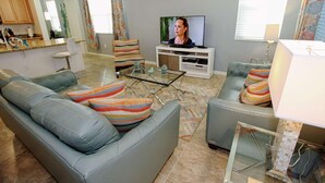 A living room with a television, two sofas, a coffee table, and a kitchen area in the background. - 3207 Compass Bay (Kissimmee)
