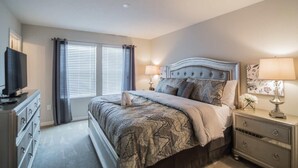 Une chambre à coucher comprenant un lit, des tables de chevet, une commode, un téléviseur et une fenêtre avec des stores.