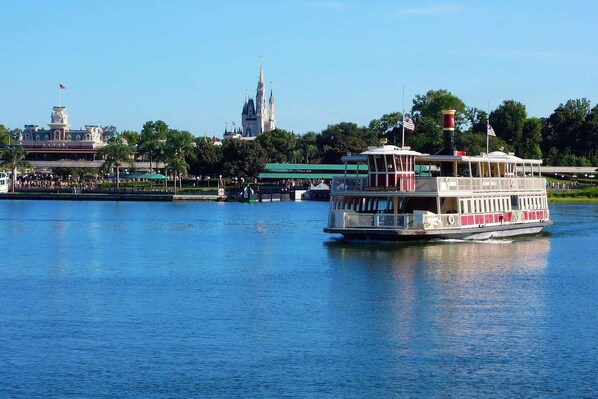 A riverboat with a white and red color scheme, docked near a large castle-like structure with spires.