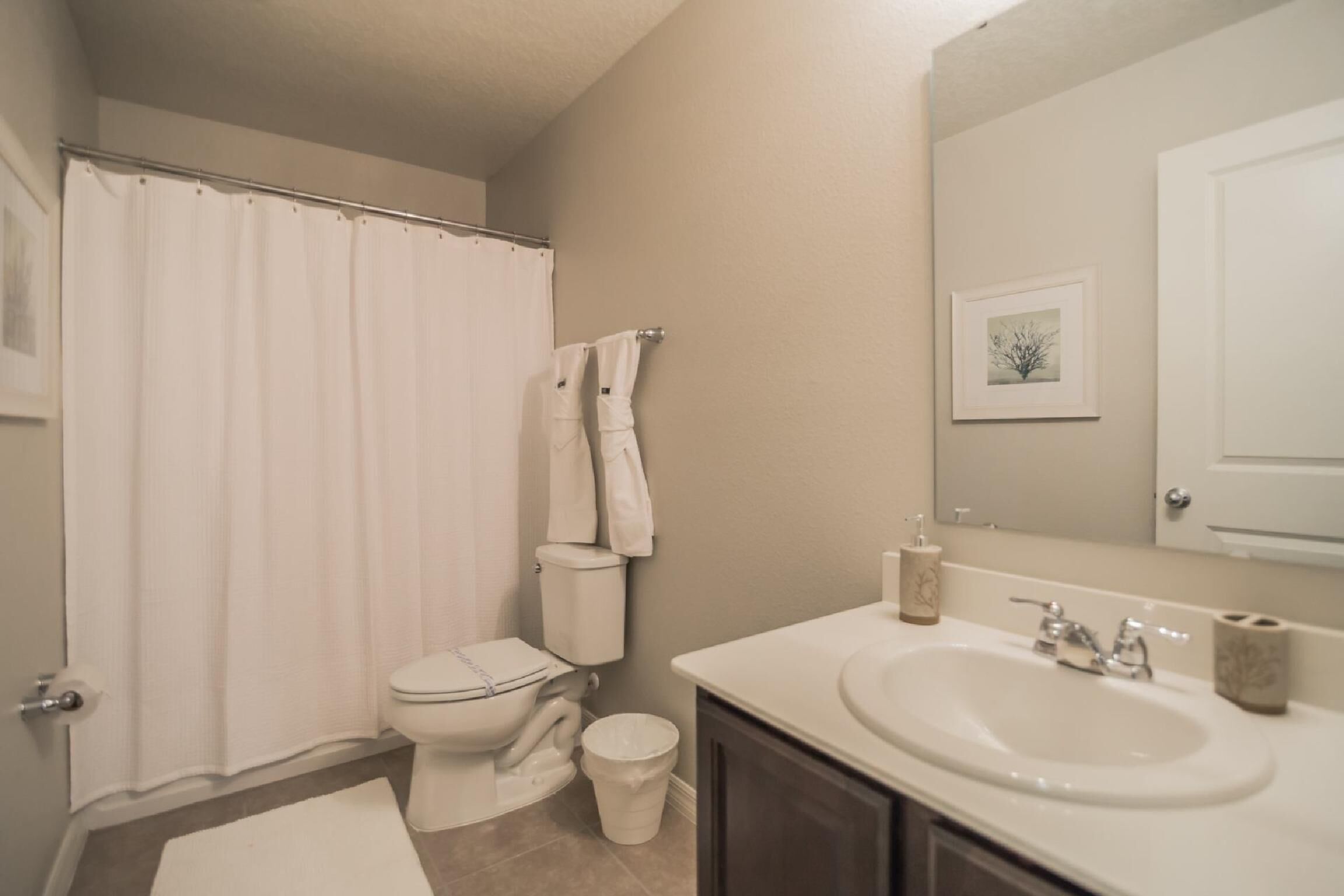 A bathroom with a toilet, shower curtain, sink, and a framed picture on the wall.