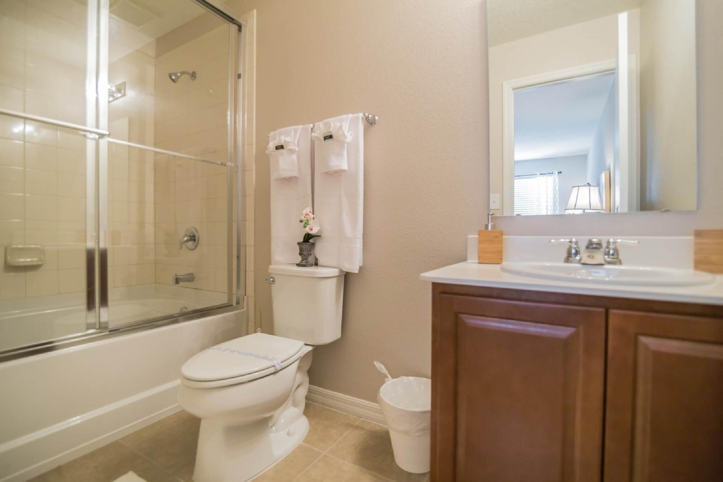 A bathroom with a glass-enclosed shower, a toilet, a sink, and wooden cabinets.