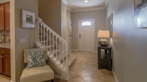 A hallway with a staircase, a door, a small table with a lamp, and a bench.