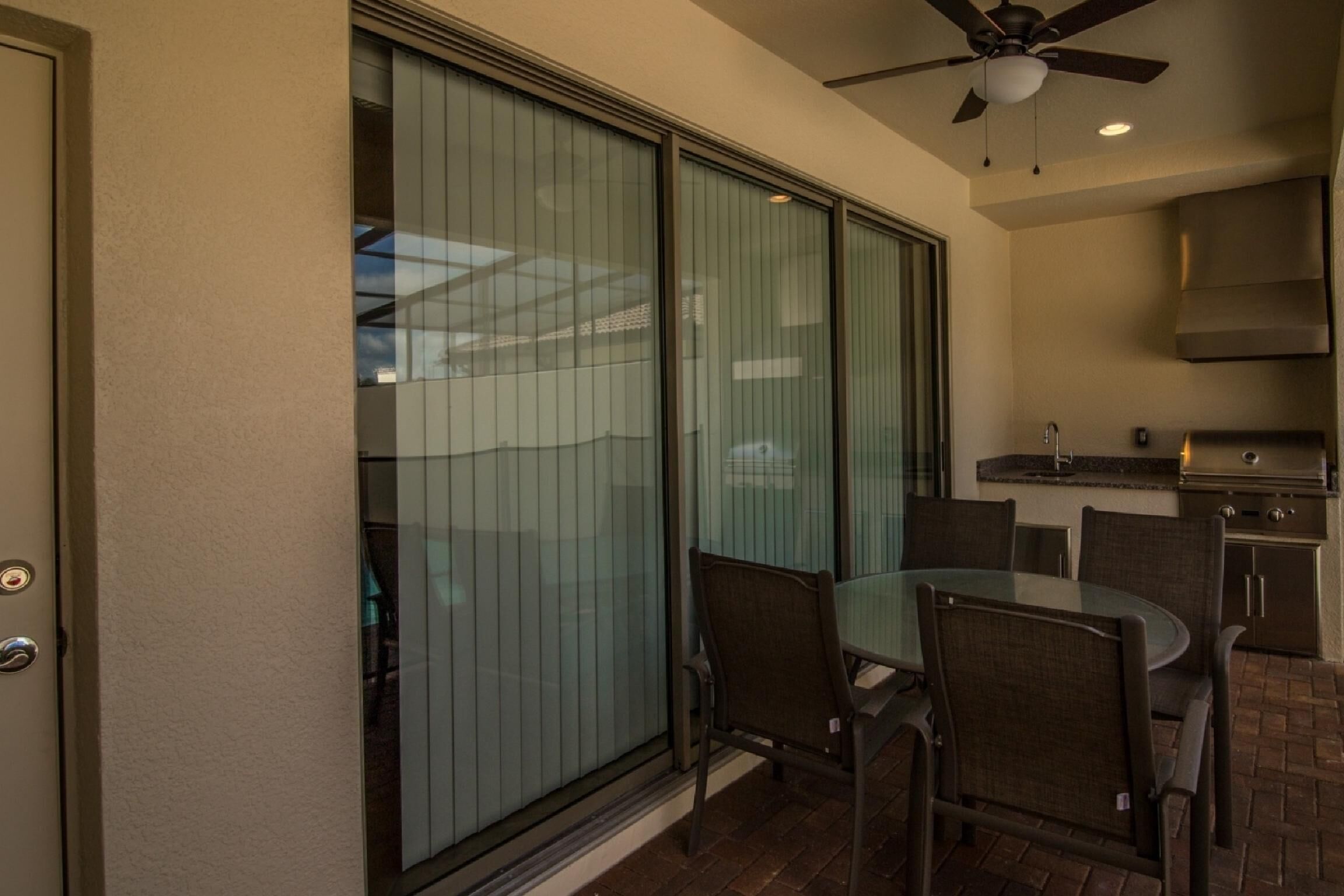 A patio area with a glass door, a ceiling fan, a round table with chairs, and a kitchen area with a grill.