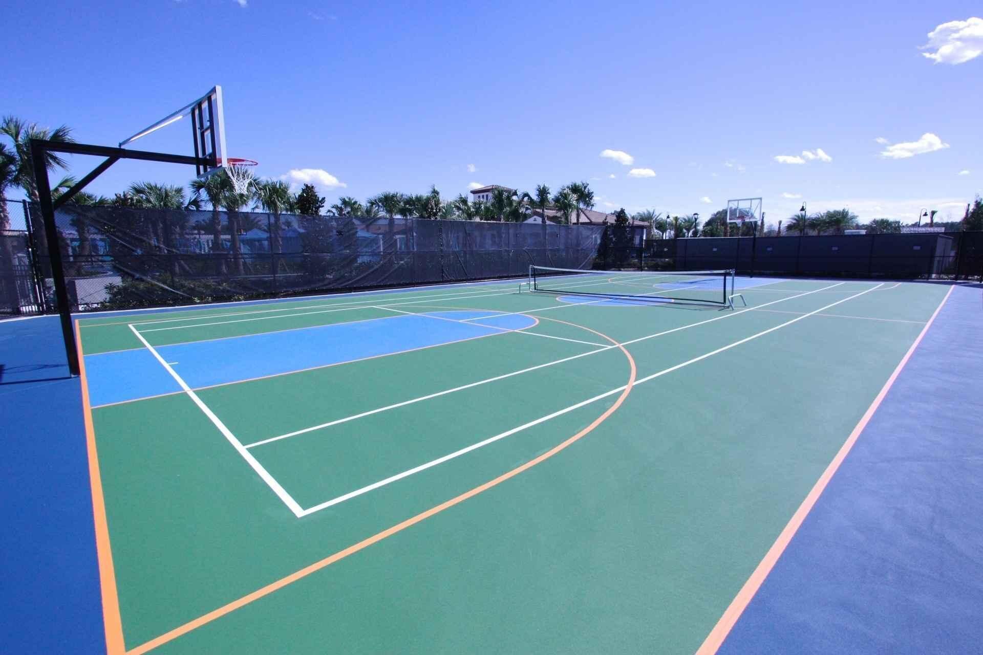 An outdoor basketball court with a net, surrounded by a fence and palm trees.