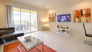 Amplia sala de estar con puerta de cristal que da a un patio, sofá de cuero, mesa de centro de mármol y televisor de pantalla plana montado en la pared.