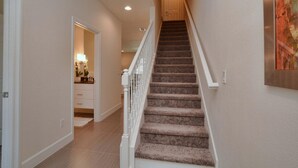 Un escalier recouvert de moquette, avec des rampes blanches, mène à une porte située en haut.