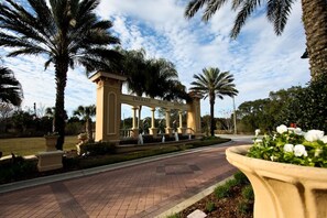 A gated entrance with a sign reading "Emerald Island Resort" surrounded by palm trees and a paved pathway.