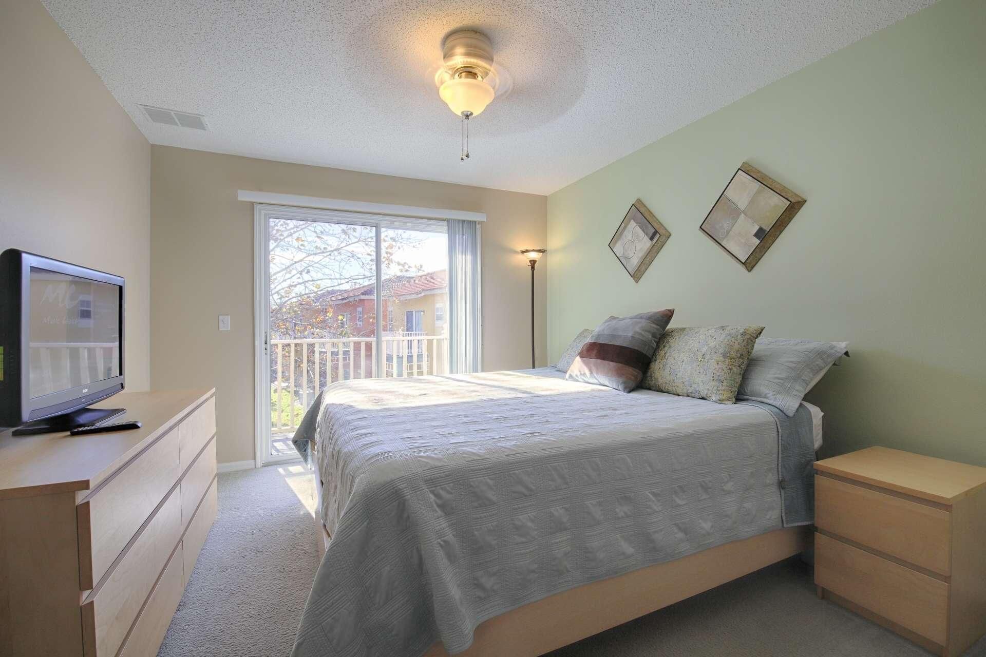 A bedroom with a bed, a TV, a desk, and a balcony.