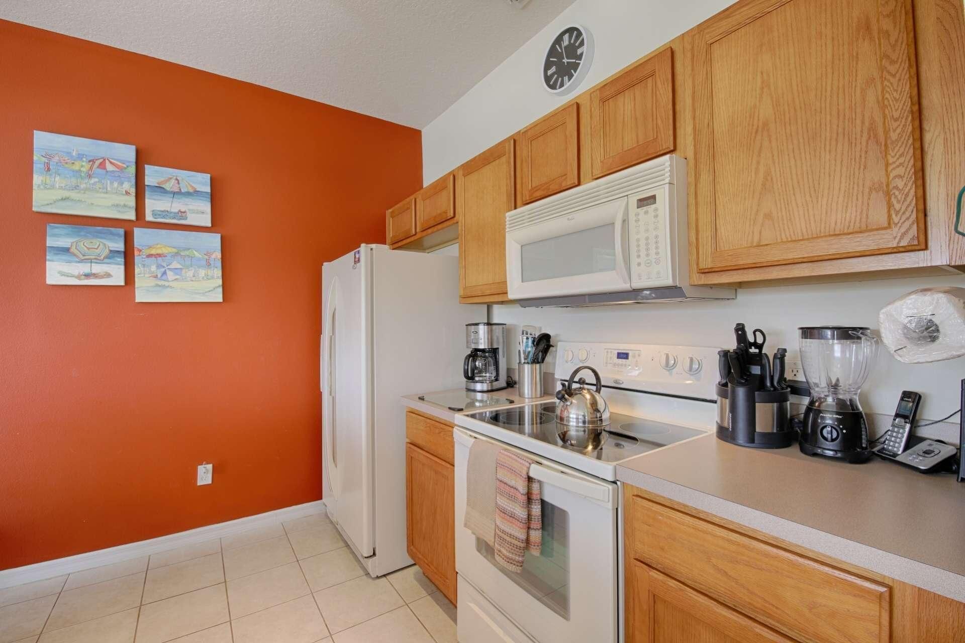 A kitchen with wooden cabinets, a white refrigerator, a microwave, a stove, and a coffee maker. There are four paintings on the wall.