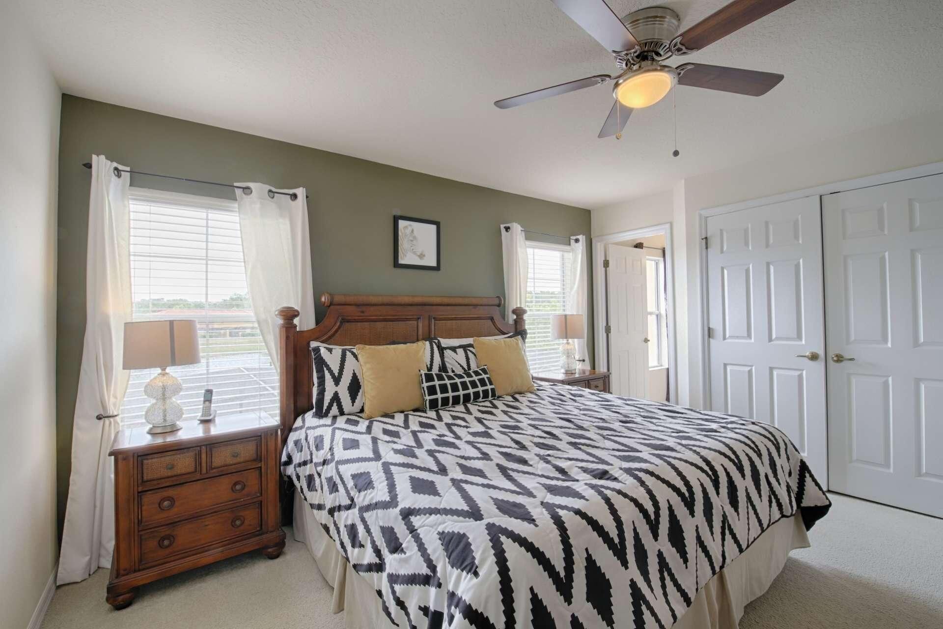 A bedroom with a bed, a nightstand, a ceiling fan, and a door.