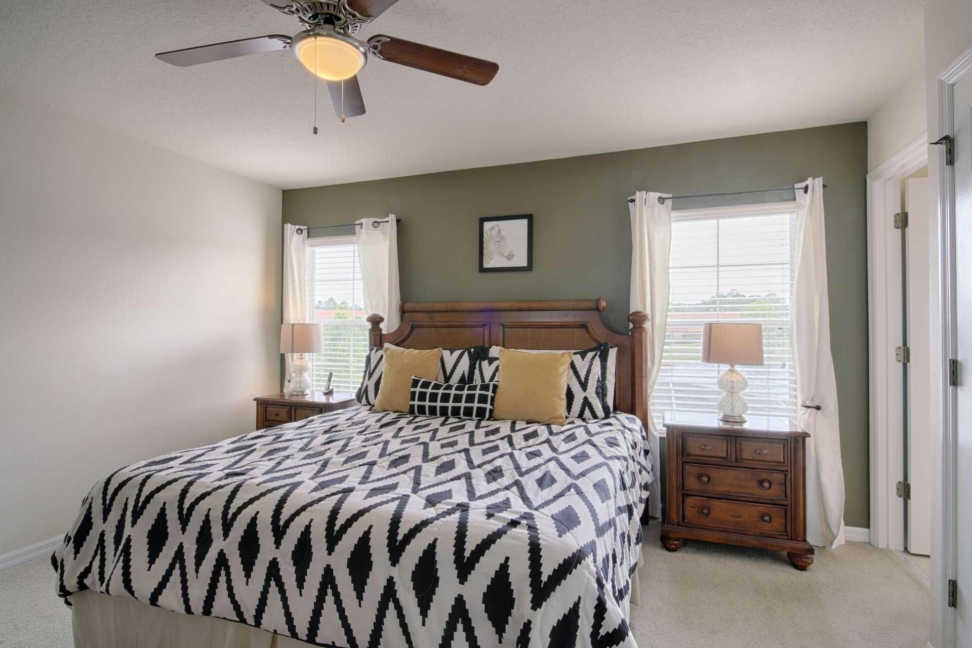 A bedroom with a bed, two bedside tables, a ceiling fan, and a window with curtains.