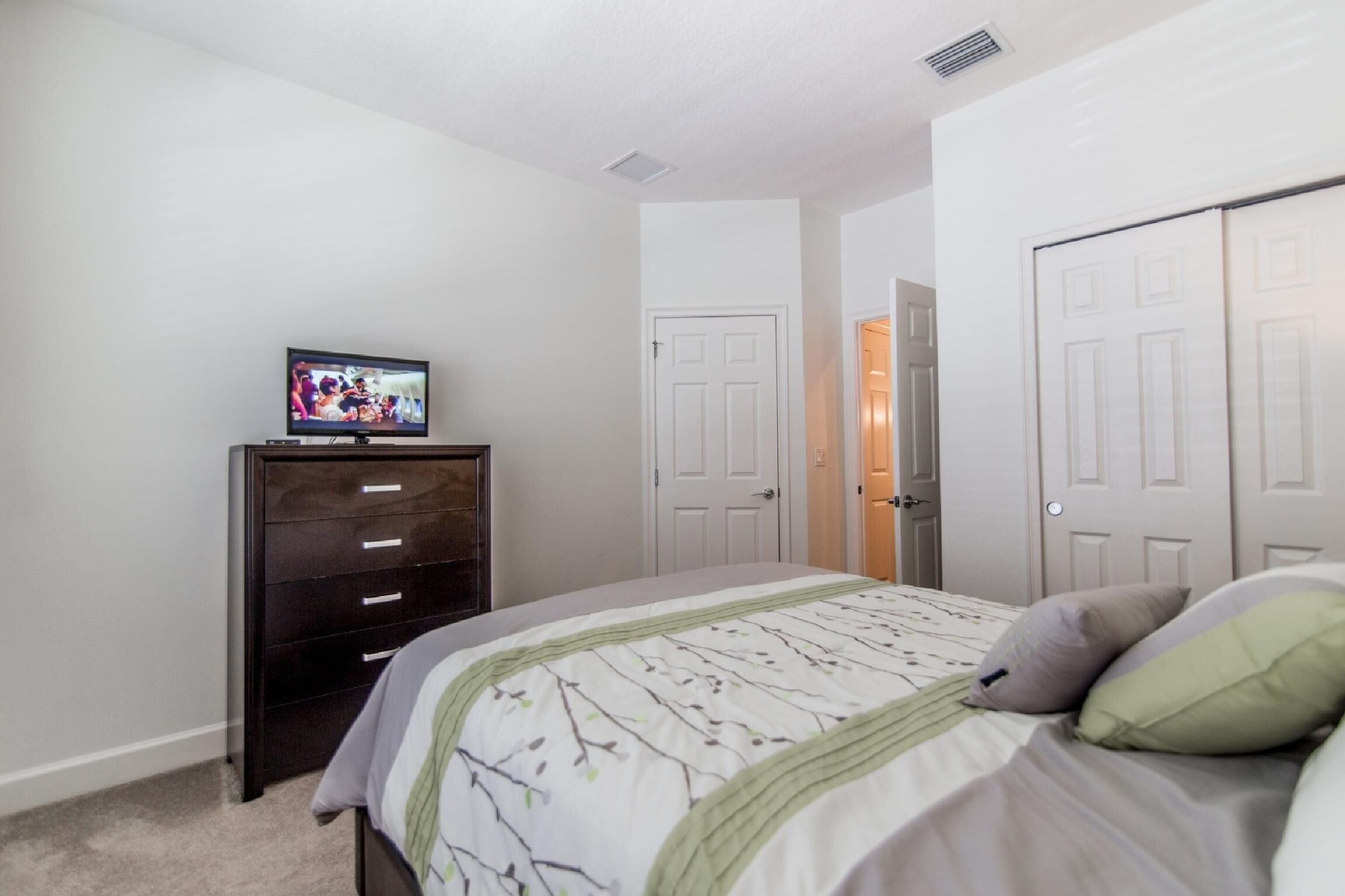 Un dormitorio con cama, cómoda, televisor y dos puertas.