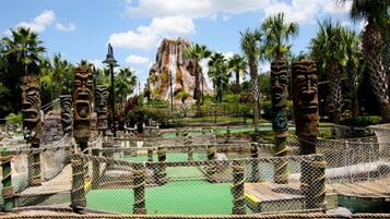 A fenced area with rope bridges, stone structures, and palm trees.