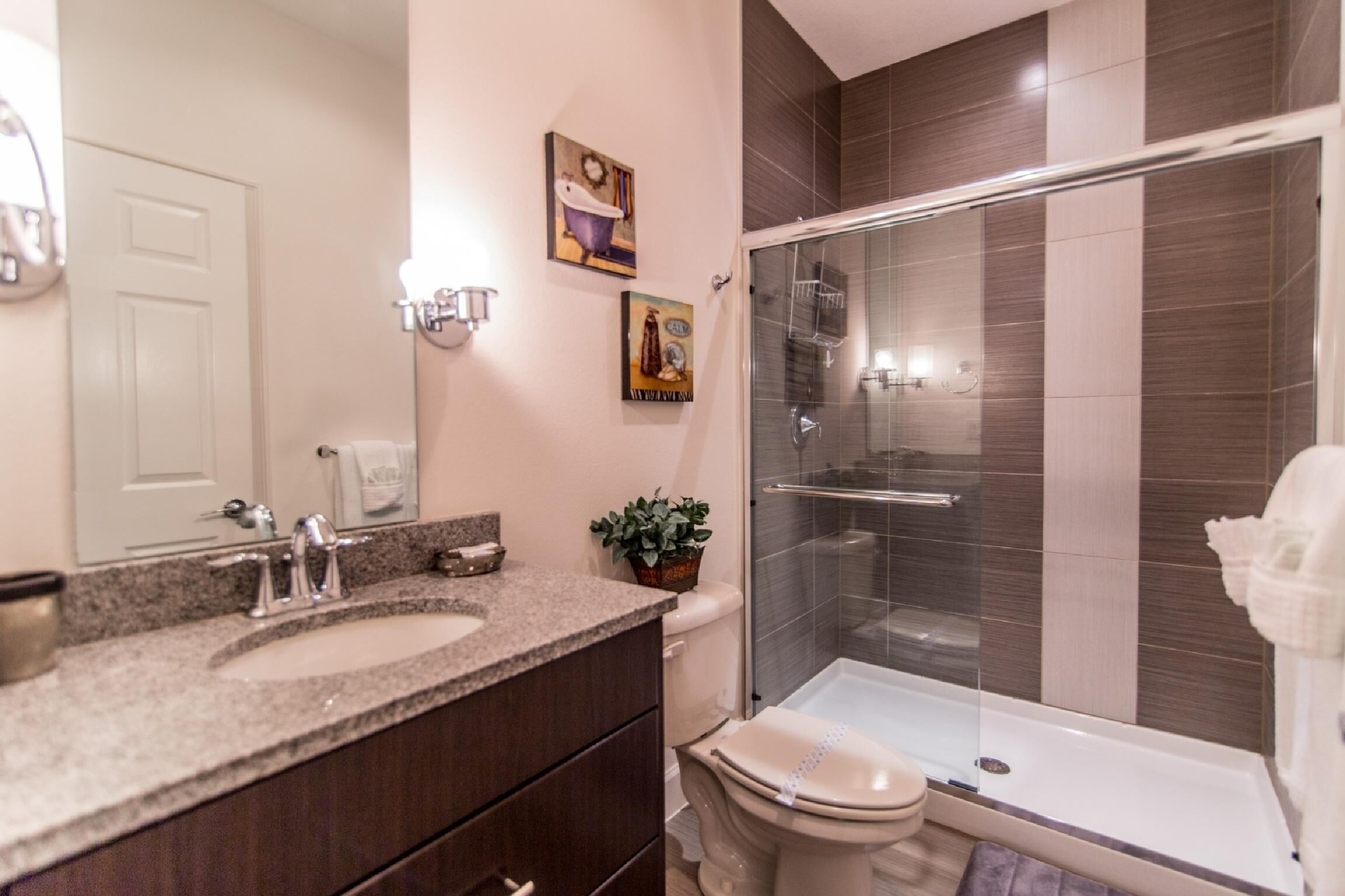 A modern bathroom with a granite countertop sink, a glass shower enclosure, and a toilet.
