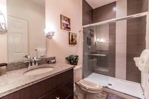 Un baño moderno con lavamanos de granito, cabina de ducha de vidrio y un inodoro.