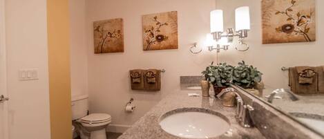 A bathroom with a sink, mirror, towel rack, toilet, and decorative wall art.