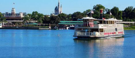 A riverboat with a white and red color scheme, docked near a large castle-like structure with spires.