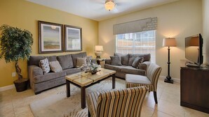 A living room with two sofas, a coffee table, a striped armchair, a floor lamp, and a television on a wooden cabinet. - 3085 Paradise Palms (Kissimmee)