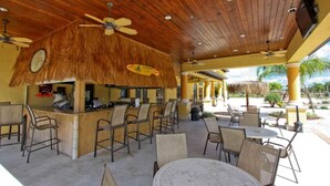 An outdoor bar area with wooden ceiling, thatched umbrellas, and multiple seating arrangements including chairs and tables. - 3085 Paradise Palms (Kissimmee)