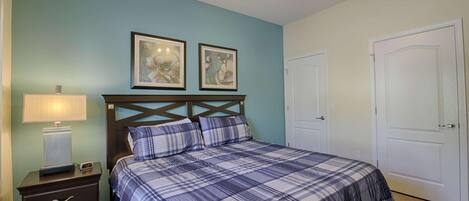 A bedroom with a bed, a nightstand, a lamp, two framed pictures, and two doors.