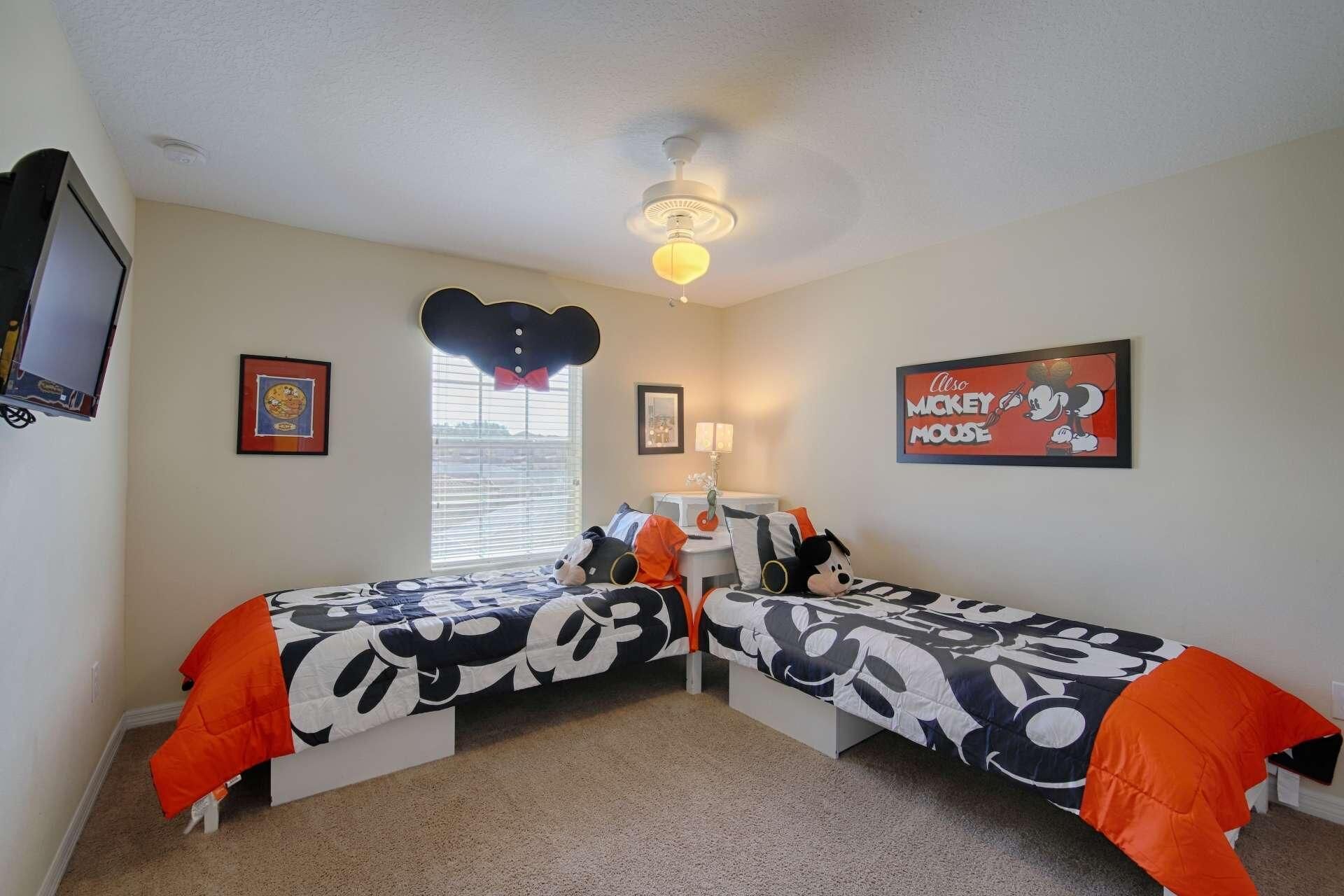 A bedroom with two beds, a ceiling fan, a TV, and Mickey Mouse-themed decorations.