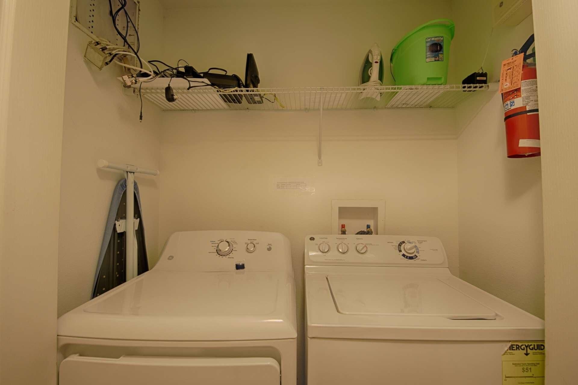 A laundry room with two white front-loading washers and dryers, a green car wash machine, and a fire extinguisher on the wall.