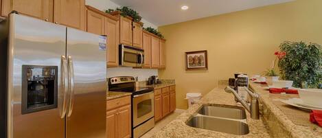 A kitchen with stainless steel appliances, wooden cabinets, granite countertops, and a sink.