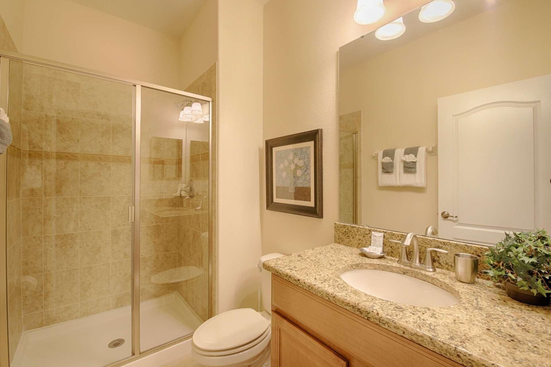 A bathroom with a glass shower enclosure, a sink with a granite countertop, and a toilet.
