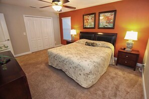 A bedroom with a bed, two nightstands, a ceiling fan, a door, and a window with blinds. - 8965 Paradise (Kissimmee)