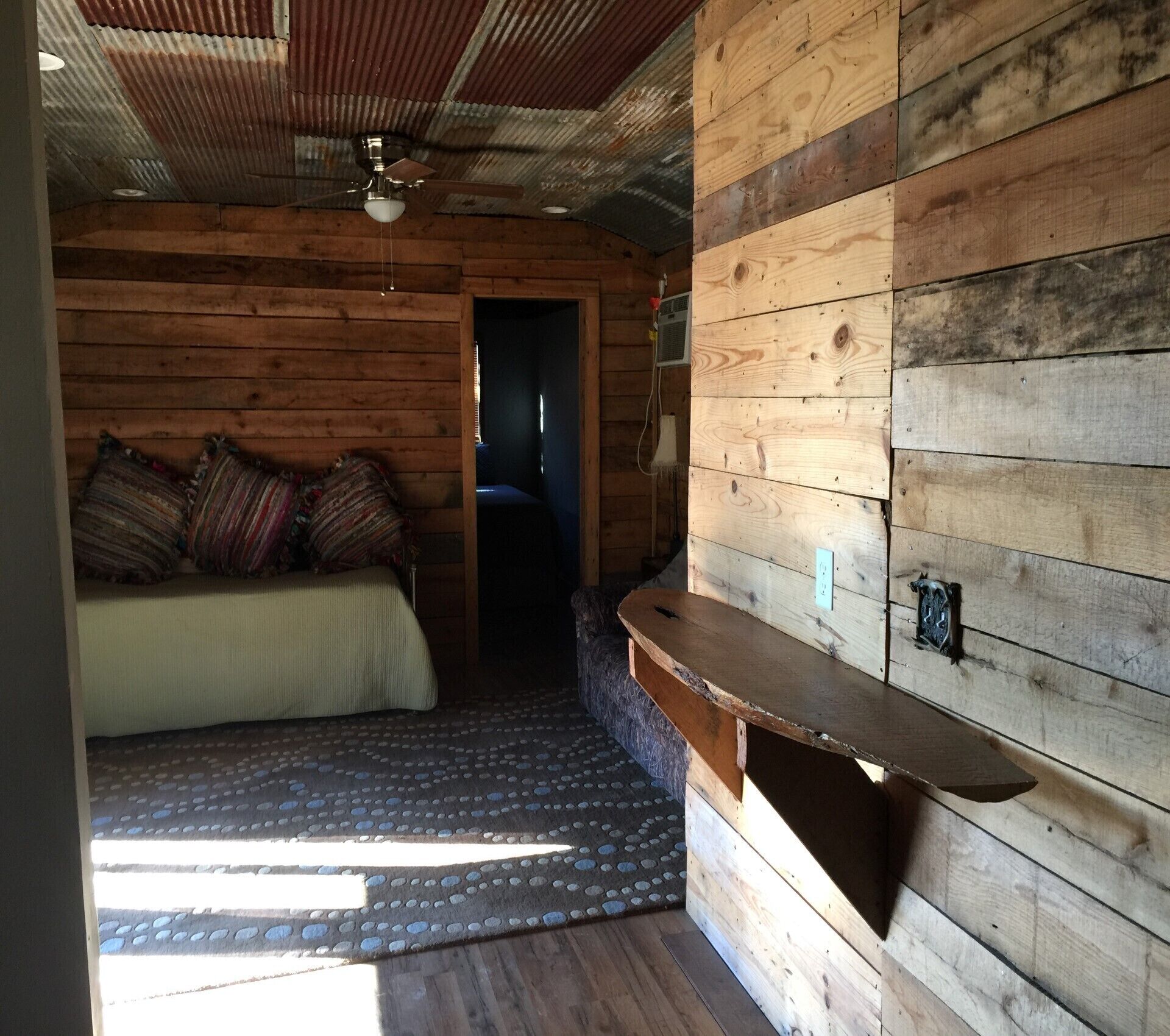 A cozy cabin room with a bed, a small bench, and a ceiling fan.