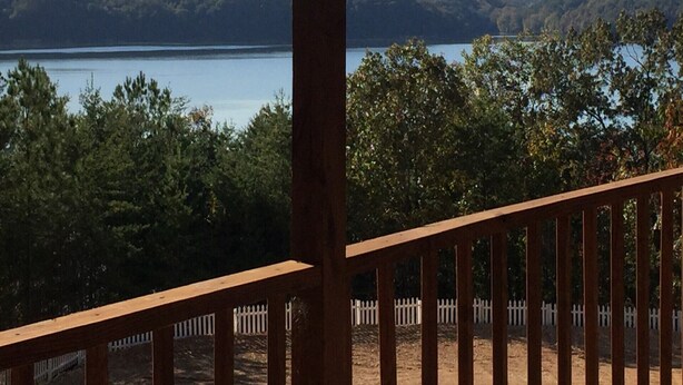 Um deck de madeira com vista para um lago e colinas arborizadas.