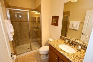 A bathroom with a glass-enclosed shower, a white toilet, a granite countertop sink, and a large mirror.