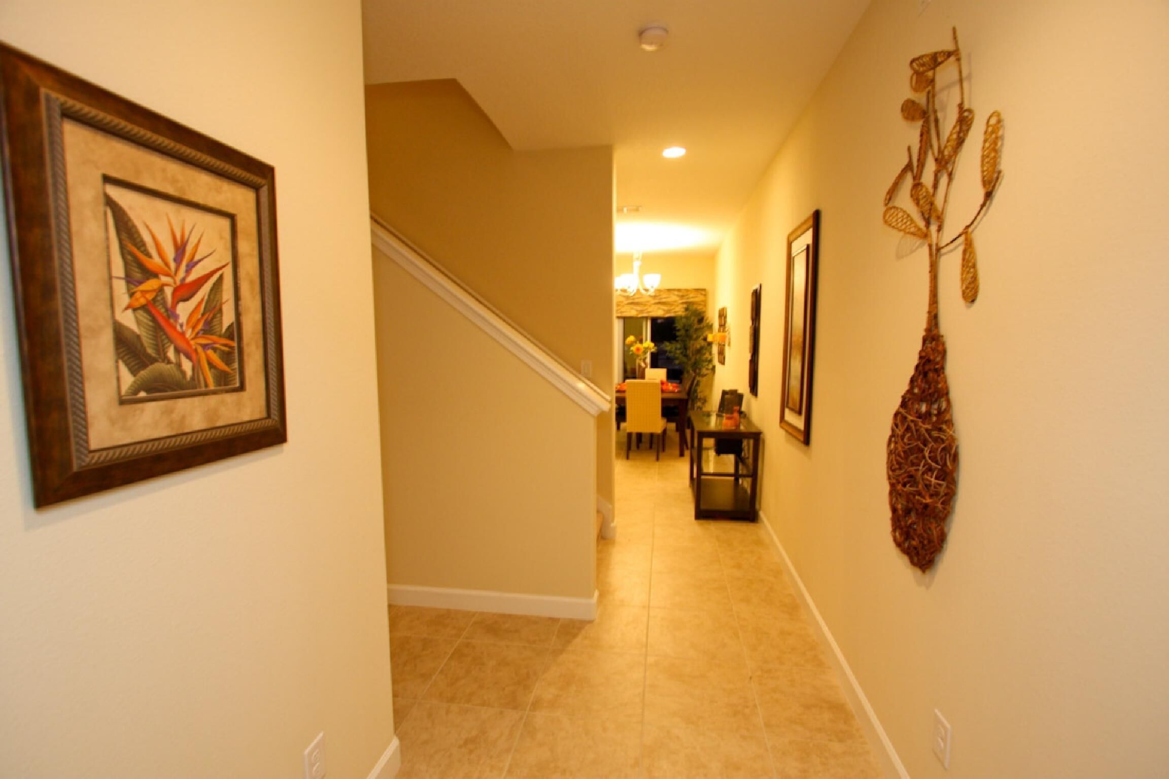 A hallway with a staircase, framed artwork, and a decorative vase.