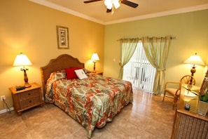 A bedroom with a bed, two bedside tables with lamps, a ceiling fan, a window with curtains, and a chair. - 2809 Oakwater (Kissimmee)