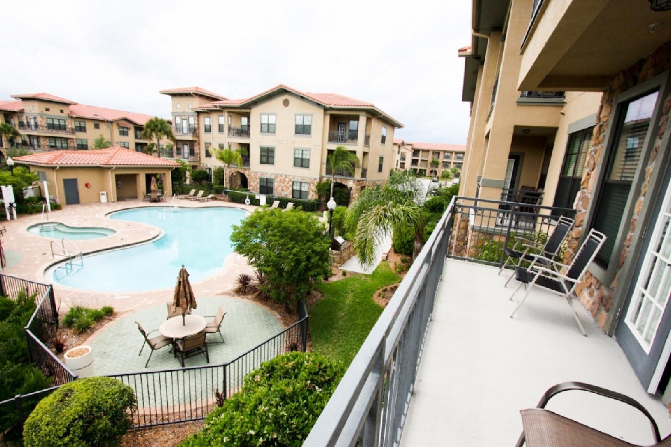 A hotel with a swimming pool, outdoor seating, and a balcony with chairs.