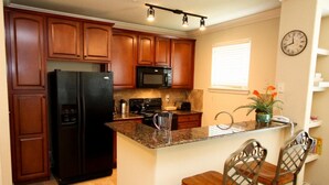 A kitchen with wooden cabinets, a black refrigerator, a microwave, and a sink. There are two bar stools and a clock on the wall.