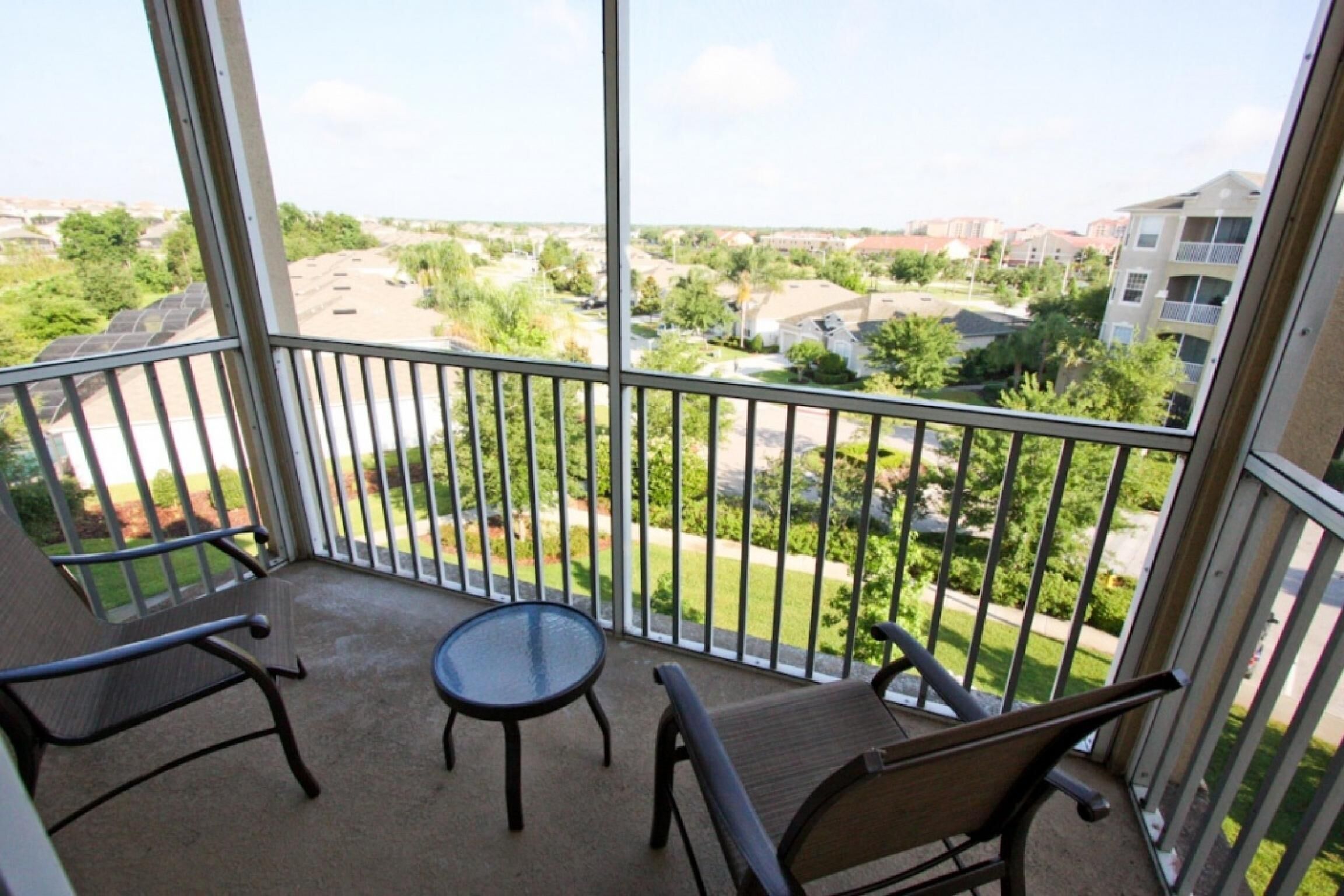 A balcony with two chairs and a small table, overlooking a residential area with houses and greenery.