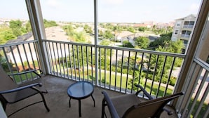 Varanda com duas cadeiras e uma mesa pequena, com vista para uma área residencial com casas e vegetação.
