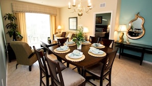 Uma sala de jantar com uma mesa de madeira posta para quatro pessoas, rodeada por cadeiras, um candelabro e um espelho na parede.