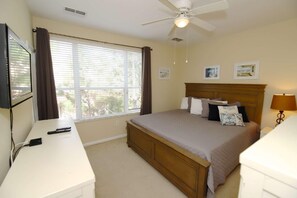 Een slaapkamer met een bed, een bureau, een plafondventilator en een raam met gordijnen.