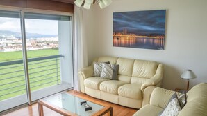 A living room with a sofa, a glass coffee table, and a painting of a cityscape.