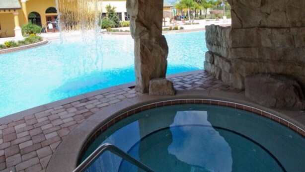 A pool area with a hot tub, stone pillars, and a view of a building with arched windows. - 8960 Paradise Palms (Kissimmee)