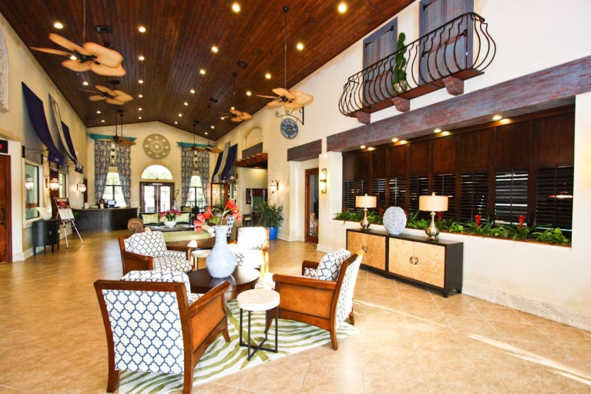 Eine geräumige Lobby mit hoher Decke, Holzbalken und einer Sitzecke mit gemusterten Stühlen und einem runden Tisch.