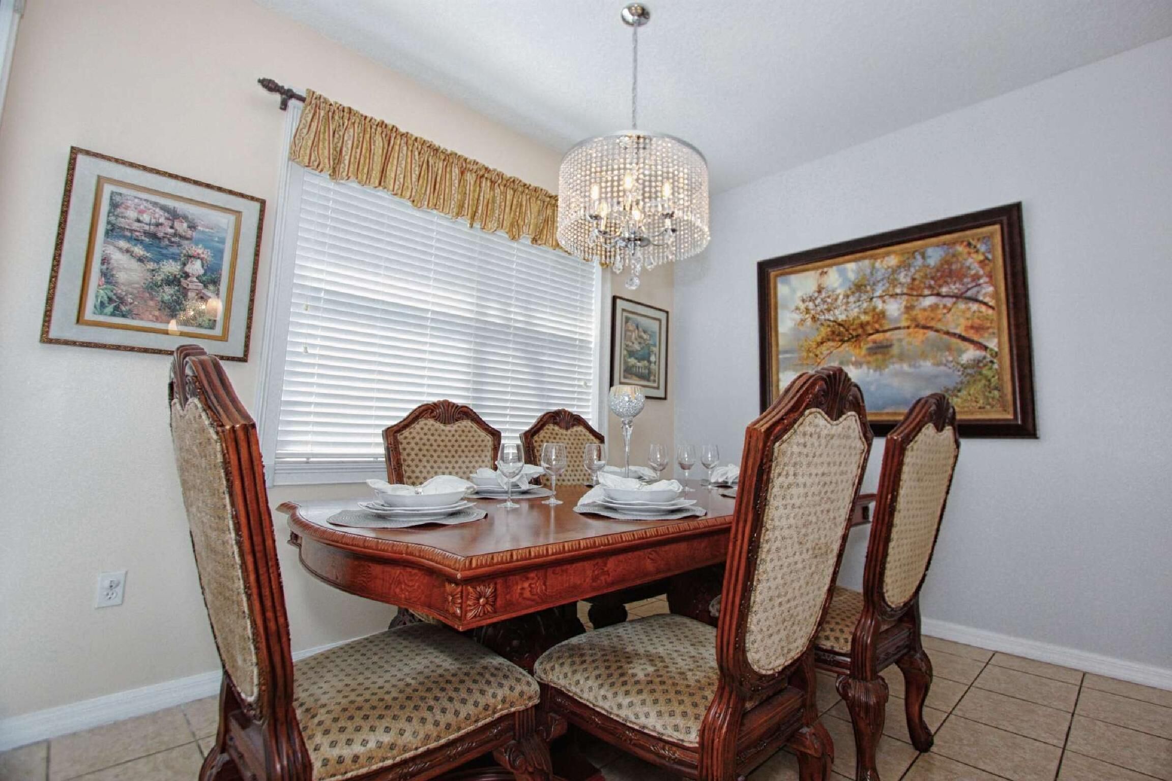 Uma sala de jantar com mesa de madeira posta para quatro pessoas, rodeada por cadeiras estofadas.