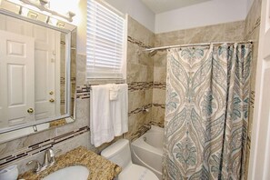 A bathroom with a sink, toilet, and bathtub. There is a window with blinds, a towel hanging on the wall, and a shower curtain with a pattern. - 329 Windwood Bay (Davenport)