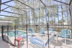 A covered outdoor area with a pool, lounge chairs, and a red chair.