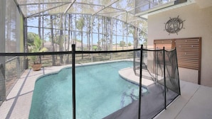 Ein Poolbereich mit Sicherheitszaun, einer Holzterrasse und Blick auf Bäume durch eine Glasdecke.