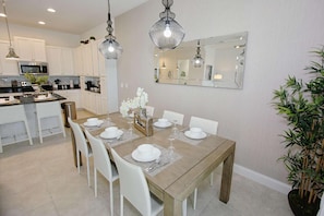 A modern kitchen with white cabinets, a dining table set for six, and a large mirror above the table. - 240 Festival (Davenport)