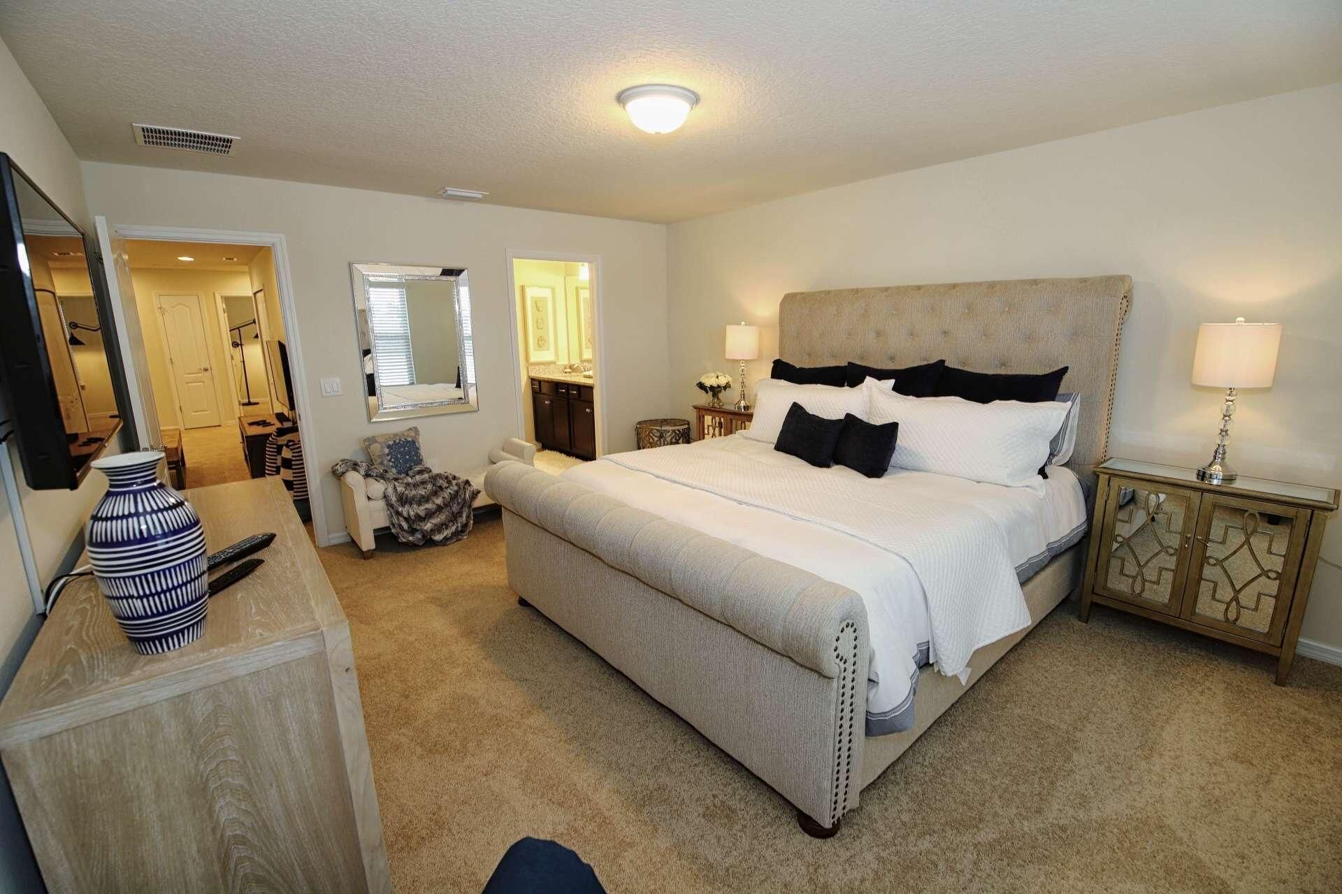 A bedroom with a large bed, a dresser, a mirror, and a nightstand with a lamp.