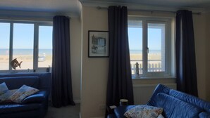 A living room with two blue sofas, a framed picture on the wall, and a view of the beach through large windows.